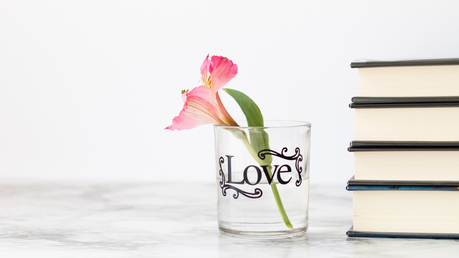 stack of books next to a glass cup containing a flower